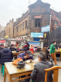 Chinese Clay Pots -（砂锅）People Enjoying Clay Pots in the Open Air with the Old Buildings of Harbin in the Background.png